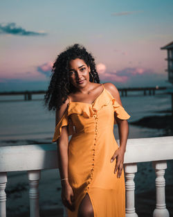 Woman standing by sea against sky during sunset