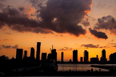 Silhouette of city against cloudy sky during sunset