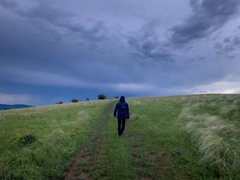 Rear view of man walking on field against sky