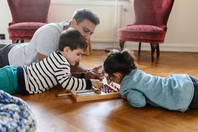 Children playing with toy while lying down with father on hardwood floor