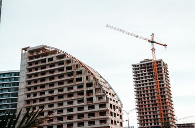 Low angle view of crane by building against sky