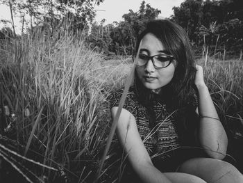 Beautiful young woman sitting on grass against trees