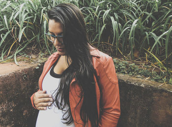 Young pregnant woman with long hair standing by retaining wall