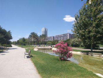 Park bench by footpath against buildings in city