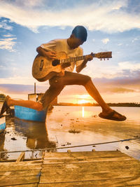 Man playing at shore against sky during sunset