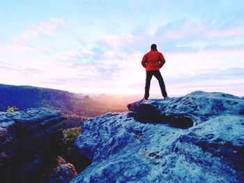 Alone tourist with cap and sporty outdoor clothes stand on cliff edge watching into national park 