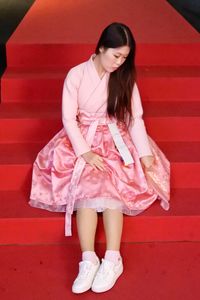 Full length of young woman sitting in pink dress on red steps