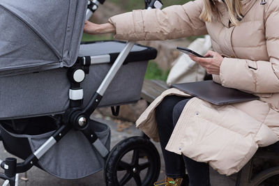 Midsection of woman holding mobile phone while sitting by baby stroller