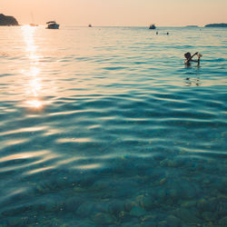 Man swimming in sea against sky during sunset