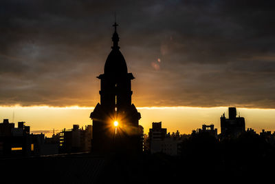 Silhouette of buildings against cloudy sky during sunset