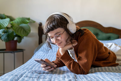 Smiling teen girl lying on bed looking funny video, film, messaging with friends in smartphone