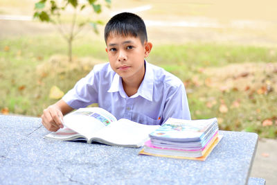 Portrait of boy reading book while studying at park