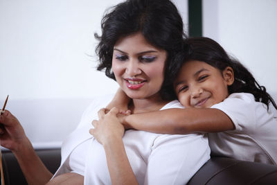 Happy daughter embracing pregnant mother sitting at home