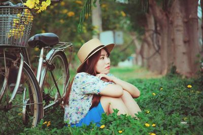 Woman with bicycle sitting on flowering field