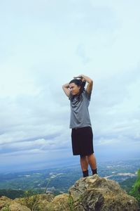 Young man standing on rock against sky