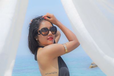 Portrait of young woman wearing sunglasses at beach against sky