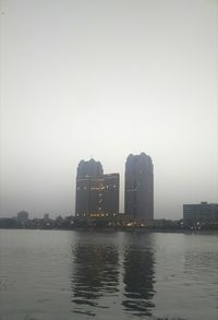 Sea by buildings against sky in city during foggy weather