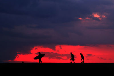 Silhouette people at beach against cloudy sky during sunset