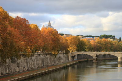 Bridge over river amidst buildings against sky during autumn