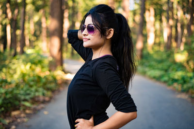 Side view of young woman wearing sunglasses standing against plants