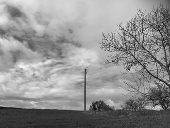Lonely electric pole in the countryside, cloudy sky, bare trees, winter season
