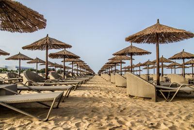 Lounge chairs and parasols on beach against clear sky