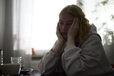 Pensive teenage girl sitting at table with head in hands