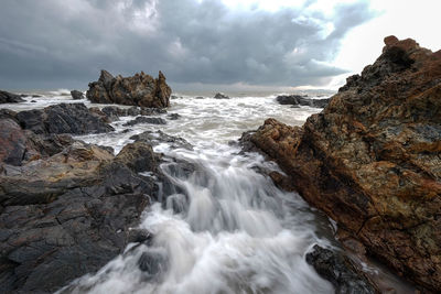 Long exposure image of waves crashing at beach against storm clouds