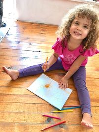 High angle portrait of girl drawing while sitting on hardwood floor