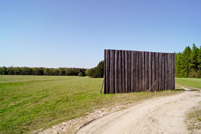Wooden fence by pathway on field against clear sky
