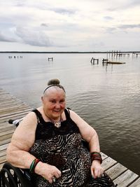 Portrait of smiling disabled woman on wheelchair by sea against cloudy sky