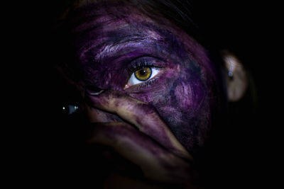 Close-up portrait of woman with messy paint on face against black background