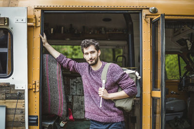 Portrait of confident young man standing with backpack against motor home doorway