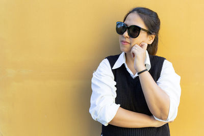 Young woman wearing sunglasses standing against yellow wall
