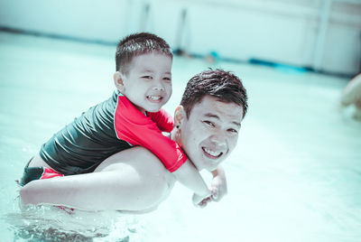 Portrait of happy father and son playing swimming pool