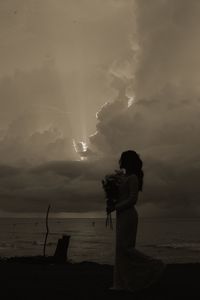 Silhouette woman standing on beach against sky during sunset