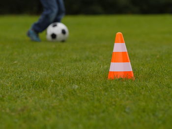 Low section of boy playing soccer by traffic cone on grassy field