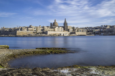 Buildings by sea against cloudy sky