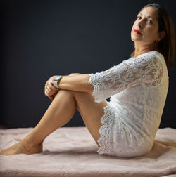 Young woman looking away while sitting against black background