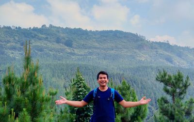 Portrait of happy man with arms outstretched standing against mountains