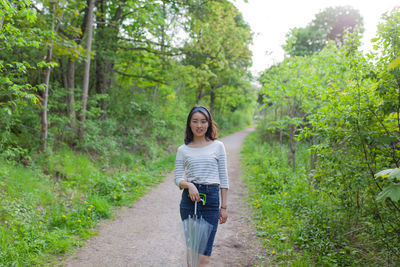 Portrait of young woman holding umbrella while standing on footpath in forest