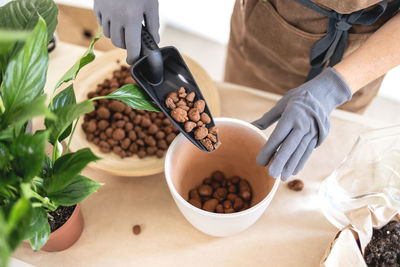 Close up of gardener hands adding pebbles in pot for transplanting houseplant