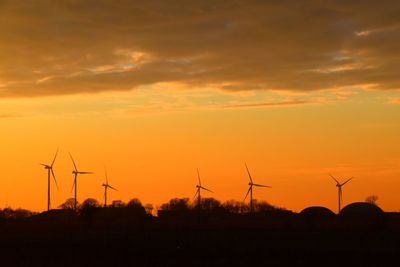 Silhouette wind turbines on field against sky during sunset