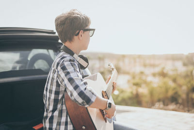 Young boy playing guitar and using smartphone outdoor. teen enjoying music