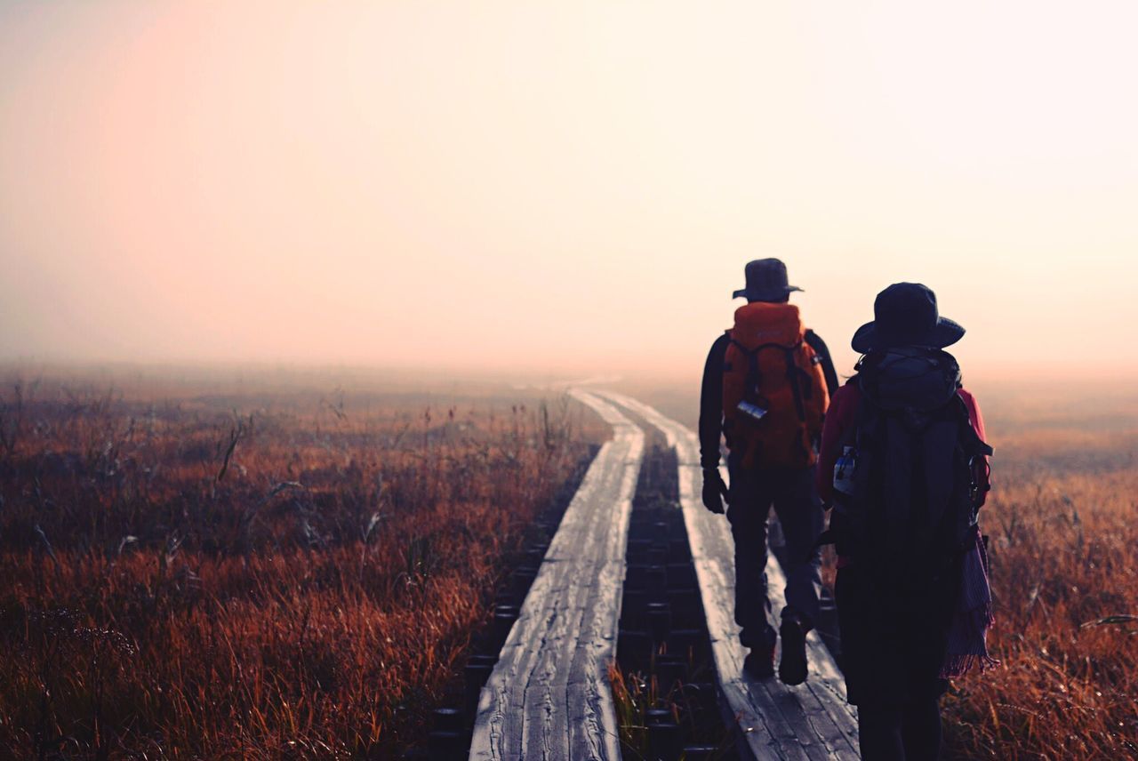 REAR VIEW OF MEN WALKING ON LANDSCAPE AGAINST SKY DURING SUNSET