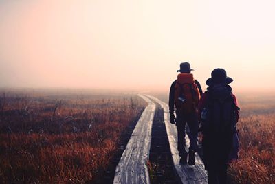 Rear view of men on landscape against sky during sunset