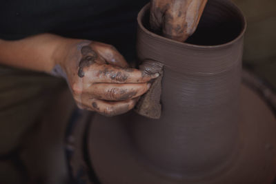 A middle-aged woman works on a potter's wheel, her face is not visible
