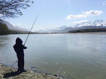 Man fishing in lake against sky