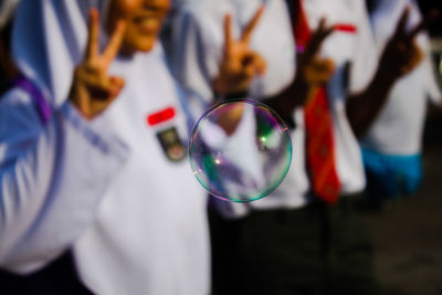 Close-up of bubble against people showing peace signs