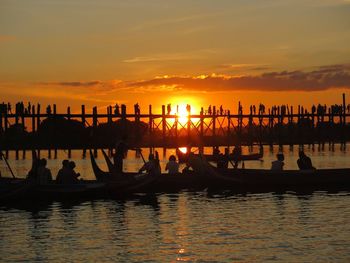 People on boat in river by u bein bridge against sky during sunset